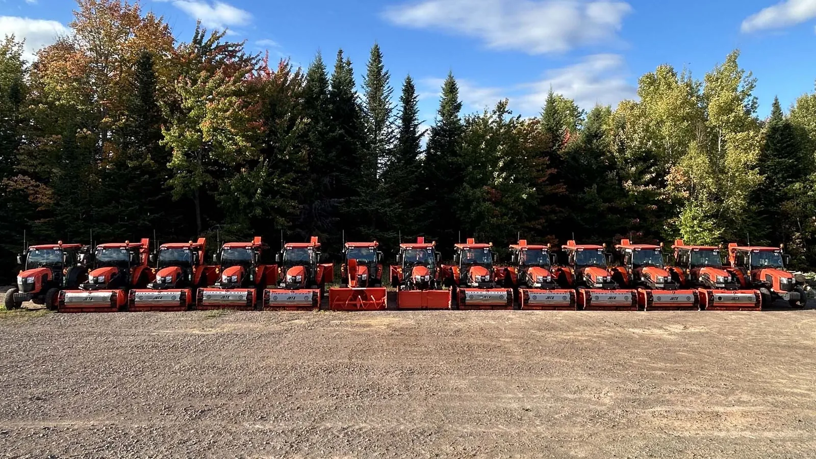 The SnowTechs fleet of orange tractors with snow blowers lined up in front of a treeline